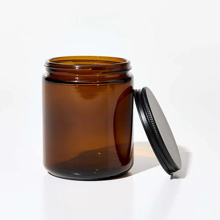 Empty amber glass candle jar with black metal lid beside it