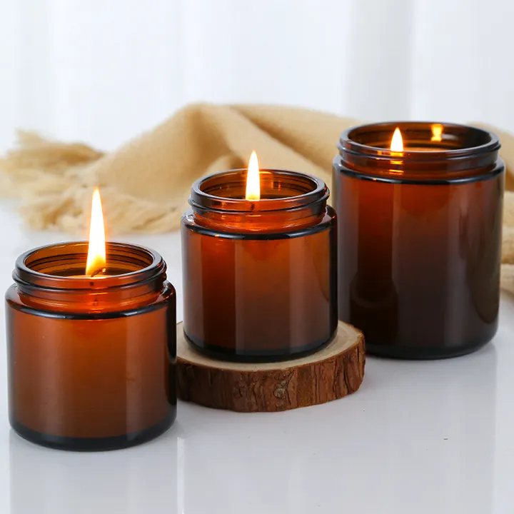 Three lit amber glass candle jars on wood slices and fabric