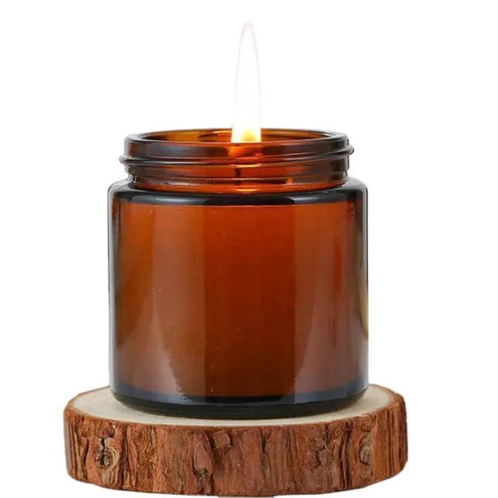 Lit amber glass candle jar on a round wood base