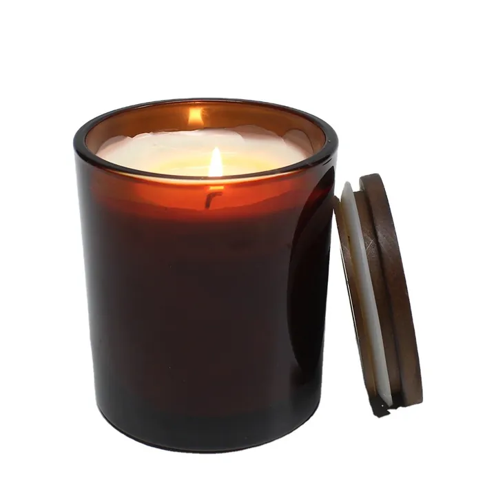 Lit dark amber glass candle jar with wood lid beside it