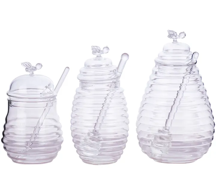 Three beehive shaped clear honey jars with bee lids and glass honey dipper