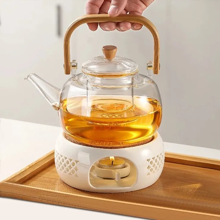Théière ronde en verre avec manche en bois, posée sur un chauffe-bougie en céramique