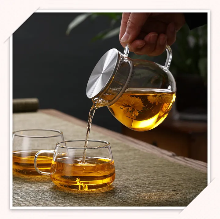 Théière ronde en verre avec couvercle-filtre en métal, servant du thé dans deux tasses en verre