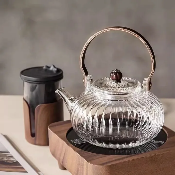 Théière en verre strié avec une poignée en bois, servant du thé sur une cuisinière électrique en bois