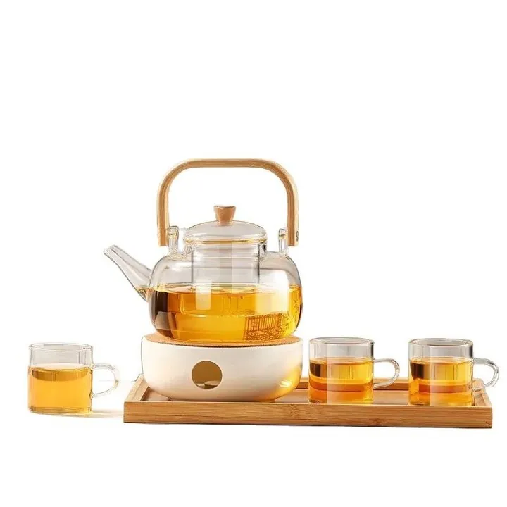 Théière en verre avec anse en bois, soucoupe chauffante en céramique et trois tasses à thé