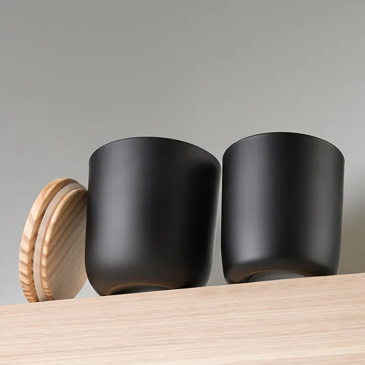 Two matte black glass candle jars with wooden lids