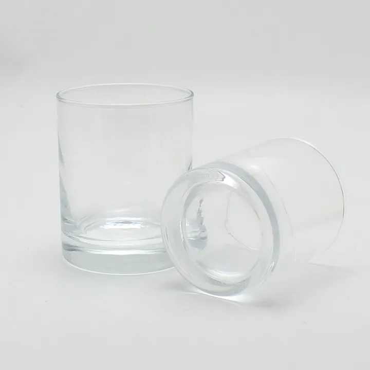 Two clear round glass candle jars with one upright and one side lying