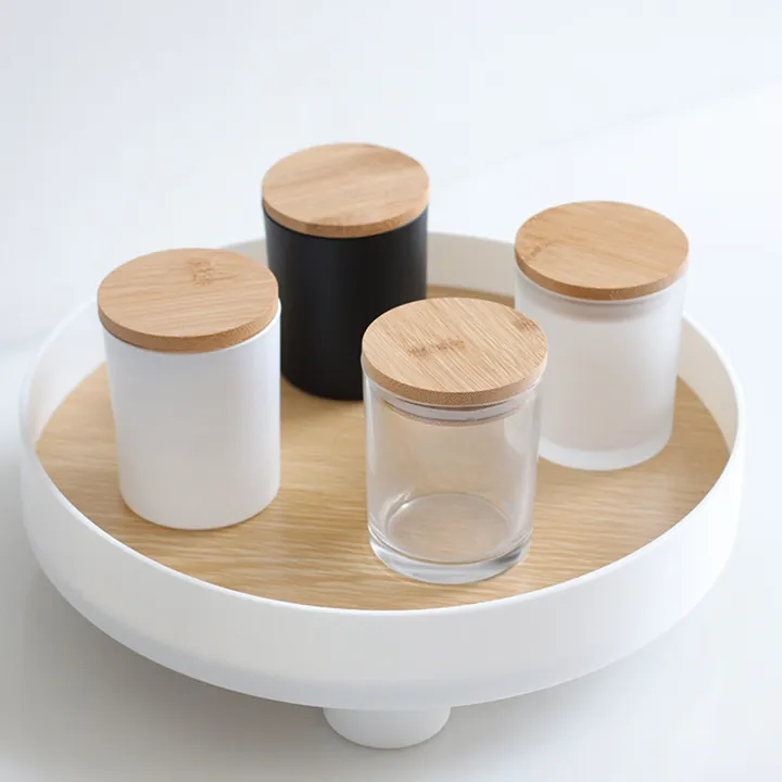 Black white and clear glass candle jars with bamboo wood lids on a round tray