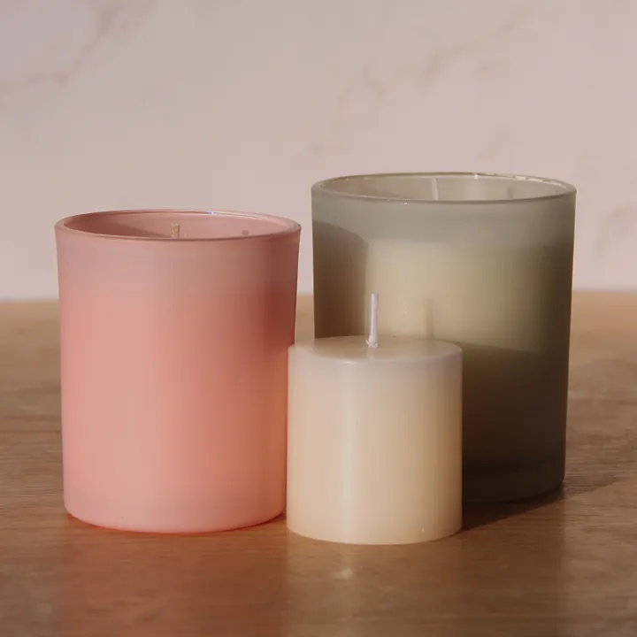 Mattglas-Kerzengläser in Rosa und Grau mit einer weißen Stumpenkerze davor