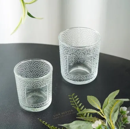 Two clear embossed glass candle jars in a plant tabletop scene