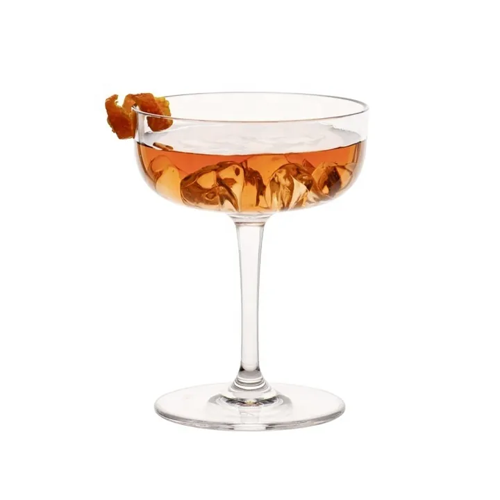Durchsichtiges Cocktailglas in Coupé-Form mit bernsteinfarbenem Eis und Garnitur