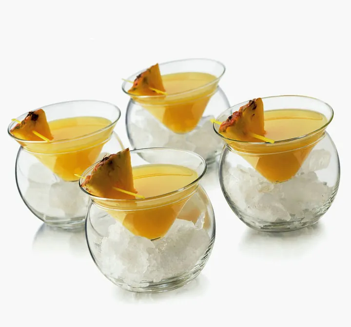 Vier runde Cocktailgläser mit gelben Getränken und zerstoßenem Eis