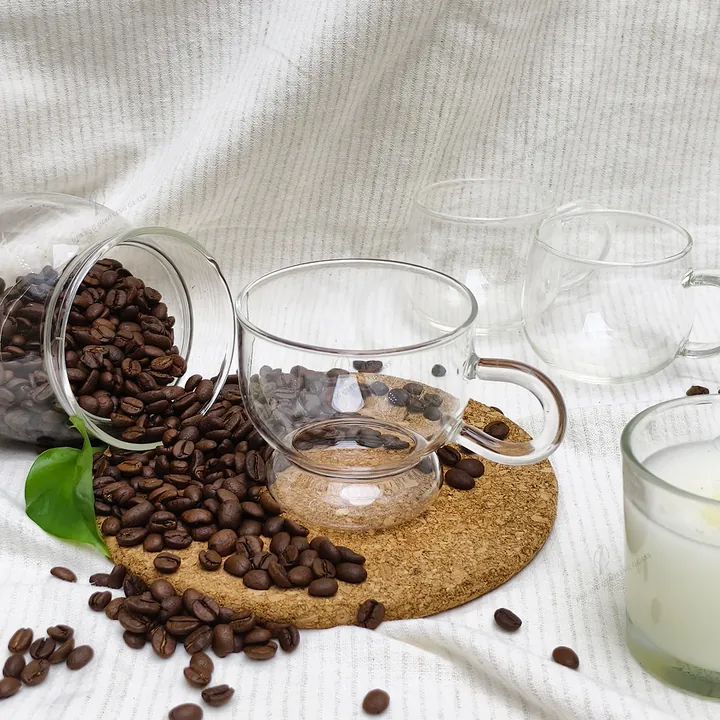 Tasse à café en verre transparent présentée avec des grains de café, un bocal de conservation et un chiffon doux