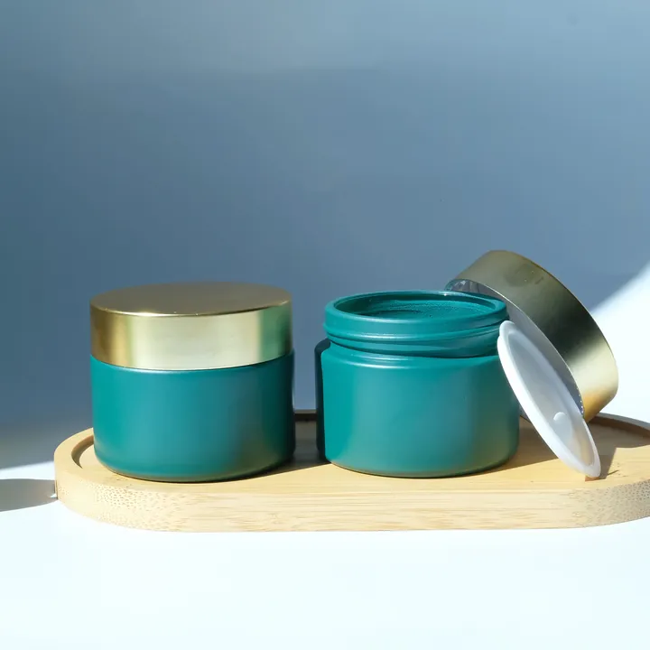 Teal cosmetic glass jars with gold lids on tray