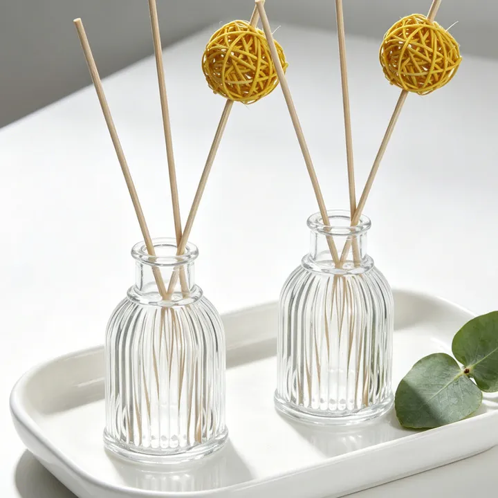 Two clear ribbed diffuser bottles with reeds and rattan balls on a white tray