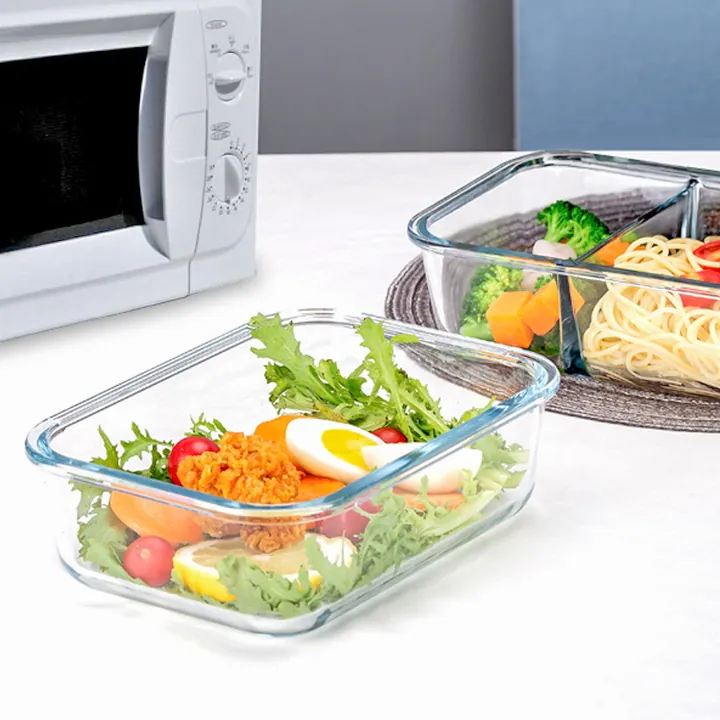 Divided glass lunch box with salad pasta and vegetables beside a microwave
