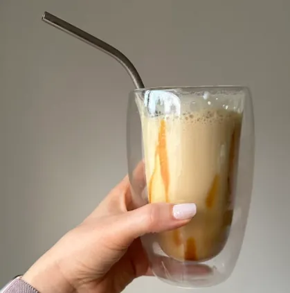 Hand holding a double wall glass tumbler with iced coffee
