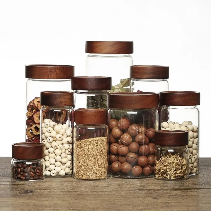 Round glass food storage jars with dark wood lids filled with beans nuts and dry foods