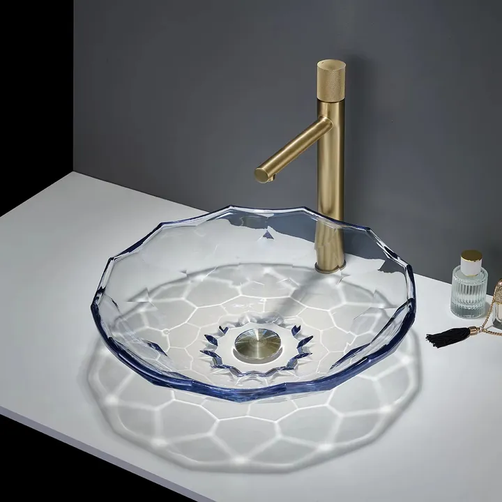 Lavabo de cristal facetado transparente con bordes azules y grifo dorado