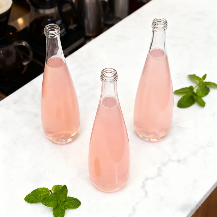 Three narrow neck beverage bottles filled with pink drinks