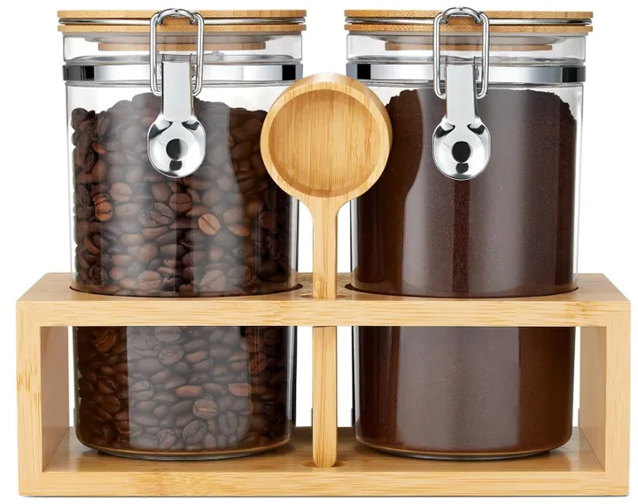 Four clamp lid glass canisters filled with coffee beans with wooden rack and spoon