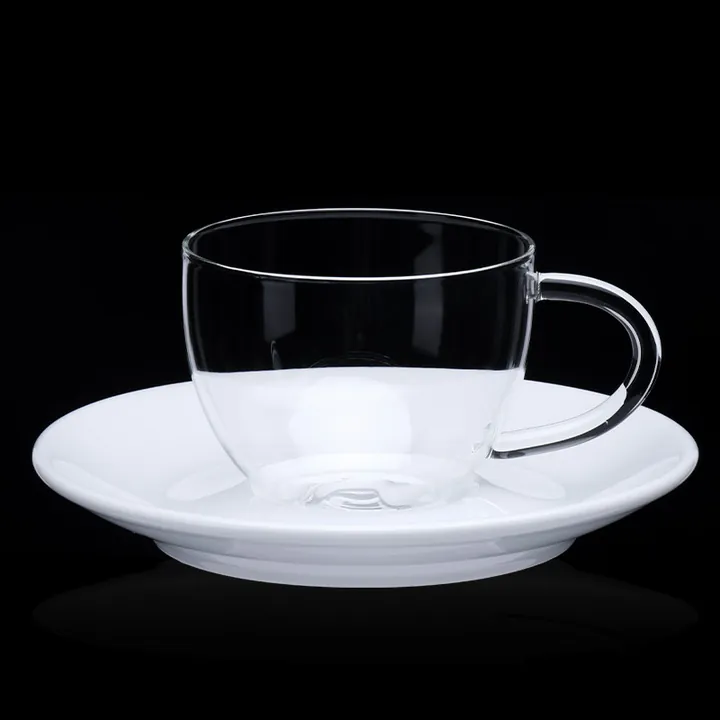 Tasse à café en verre transparent avec soucoupe blanche sur fond noir