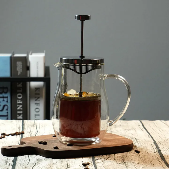 Une cafetière à piston en verre à double paroi remplie de café, posée sur une table en bois