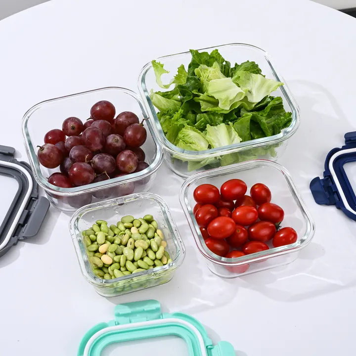 Quatre récipients alimentaires carrés en verre remplis de légumes et de fruits