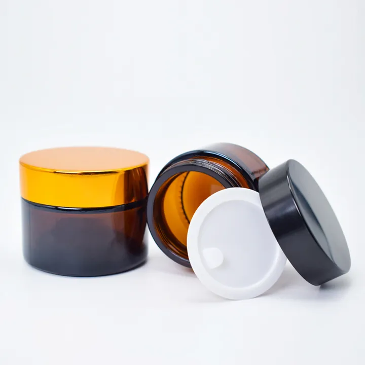 Two amber glass cream jars with gold and black lids