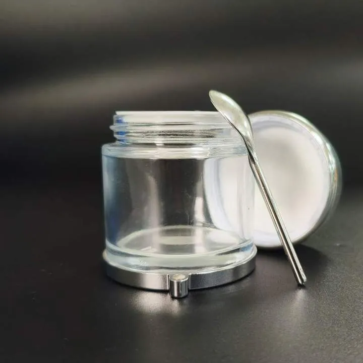 Clear round cream jar with metal base and cosmetic spoon