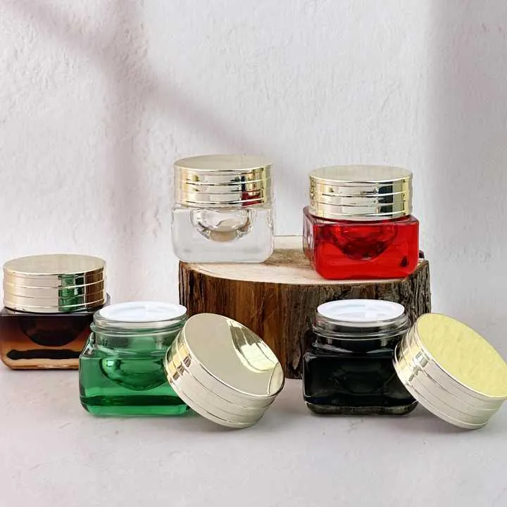 Square glass cream jars in clear, red, green, black and amber colors with gold lids