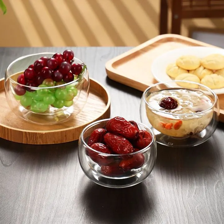 Trois coupes en verre à double paroi remplies de fruits et de desserts sur une table à manger