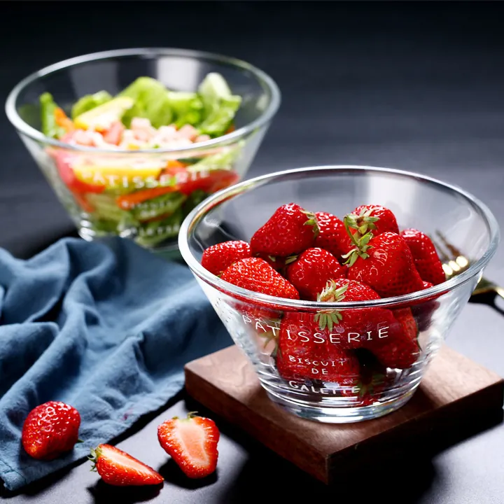 Zwei durchsichtige Glasschalen mit Obst und Salat, eine davon mit weißer Aufschrift