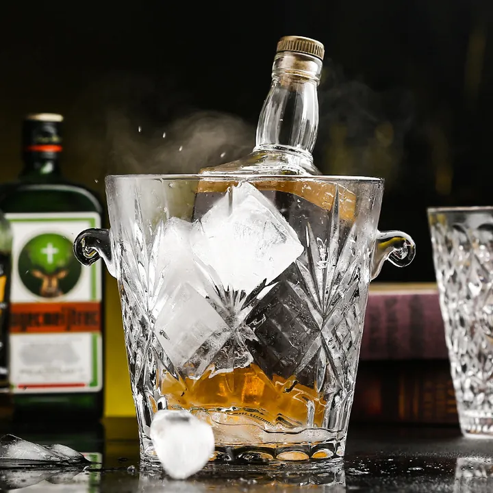 Seau à glace en verre taillé, avec des glaçons, une bouteille de vin et un verre, dans un décor de bar