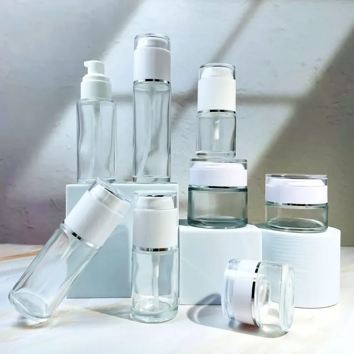 Clear glass lotion bottles spray bottles and cream jars arranged on a tabletop