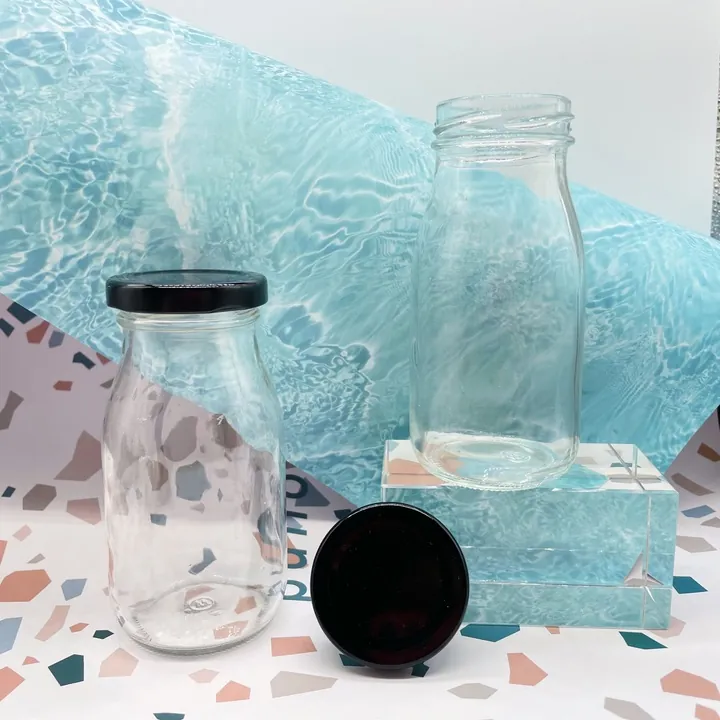 Zwei Milchflaschen aus klarem Glas mit schwarzen Verschlüssen