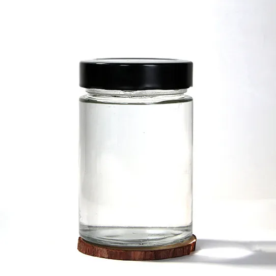 Clear cylindrical glass jar with black lid and wooden pad