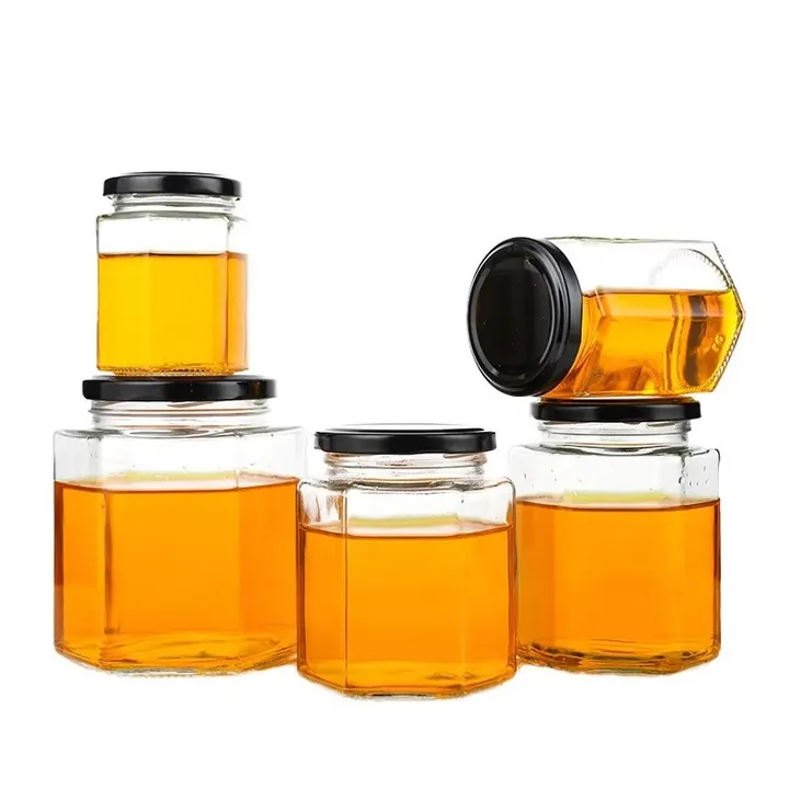 Tarros de miel de cristal hexagonales, llenos de un contenido dorado y con tapas negras