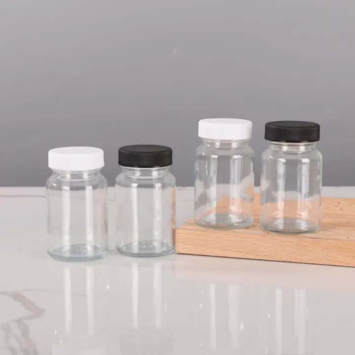 Four clear glass pill bottles with black and white caps