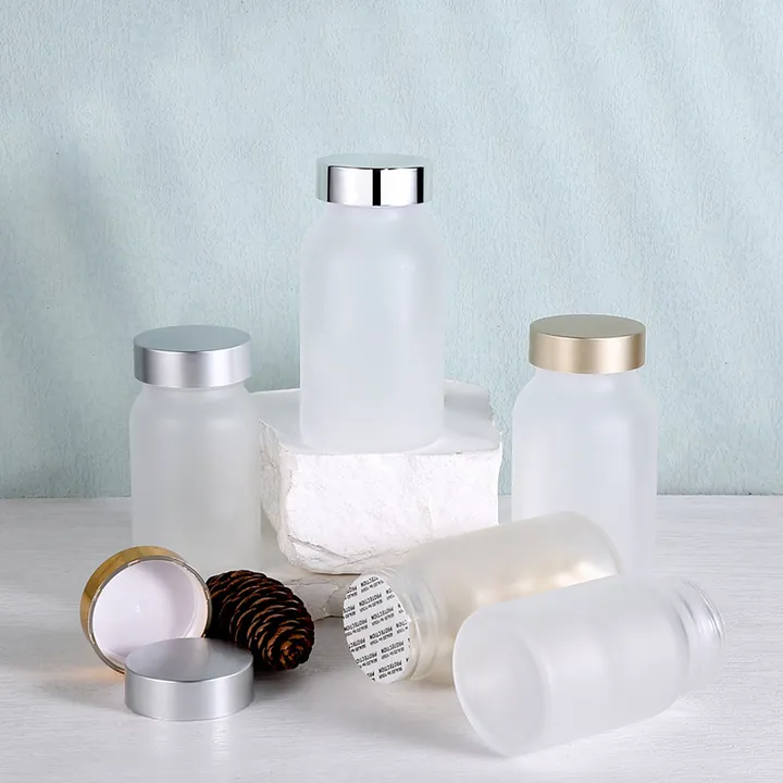 Frosted glass pill bottles with silver and gold lids on a white surface