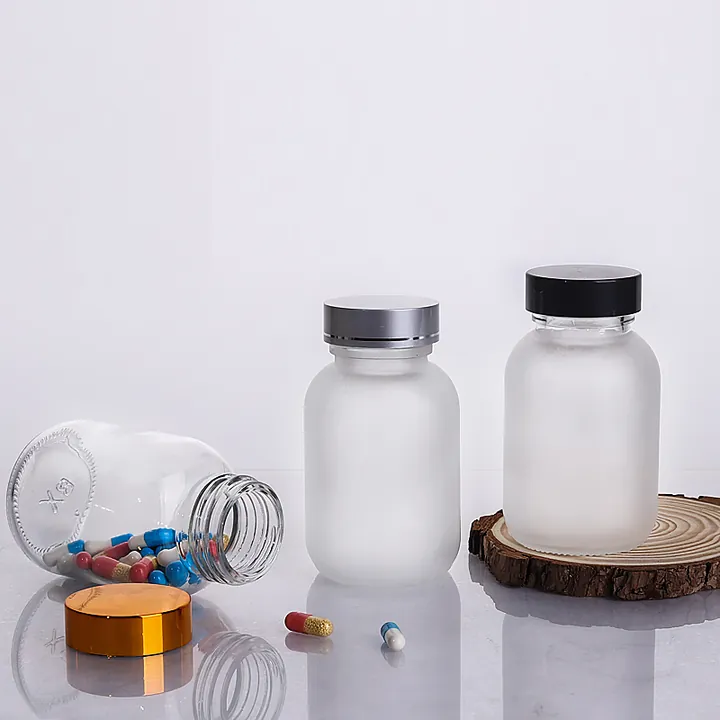 Frosted glass pill bottles with capsules and metal lids on a tabletop