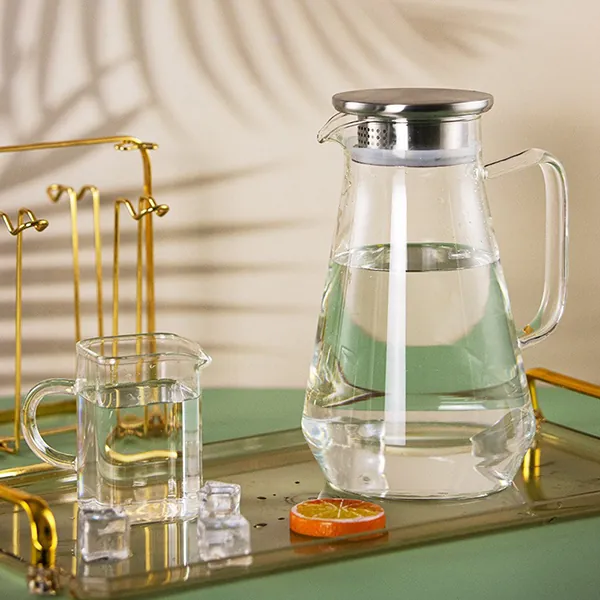 Une carafe en verre avec un couvercle en acier inoxydable, présentée avec des verres sur un plateau