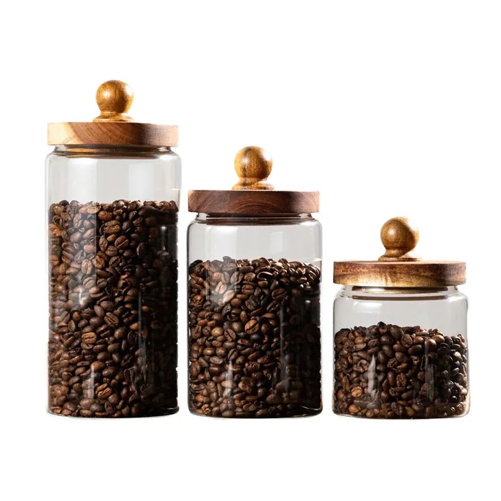 Trois bocaux de conservation en verre transparent avec des couvercles en bois à poignée ronde et des grains de café