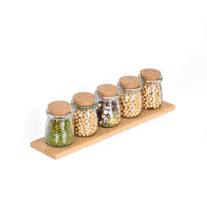 Cinq petits pots à épices en verre transparent avec des bouchons en liège sphériques et un plateau en bois