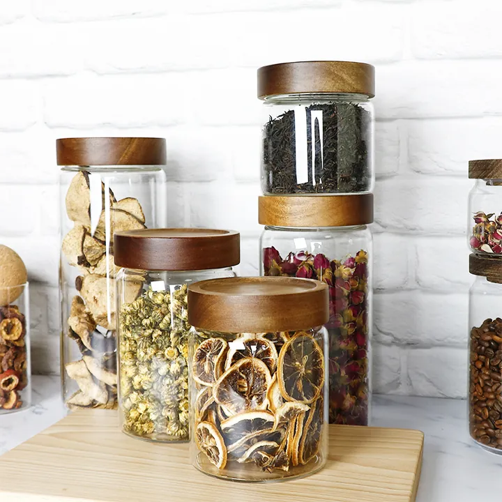 Clear glass storage jars with dark wooden lids holding dried flowers, dried fruit and tea