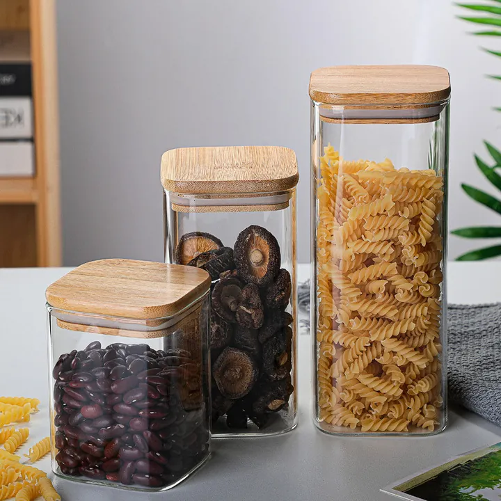 Trois bocaux de conservation carrés en verre transparent avec des couvercles en bambou et des aliments secs