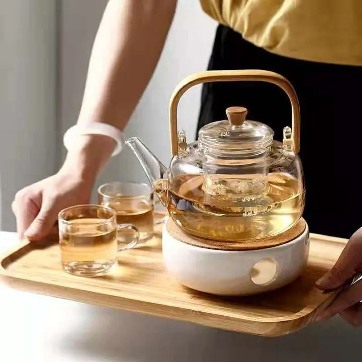 Glass teapot displayed on wooden tray with matching cups
