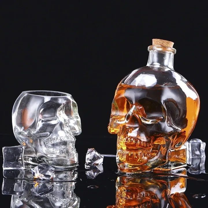 Eine Karaffe in Totenkopfform und Totenkopfgläser vor einem schwarzen, spiegelnden Hintergrund