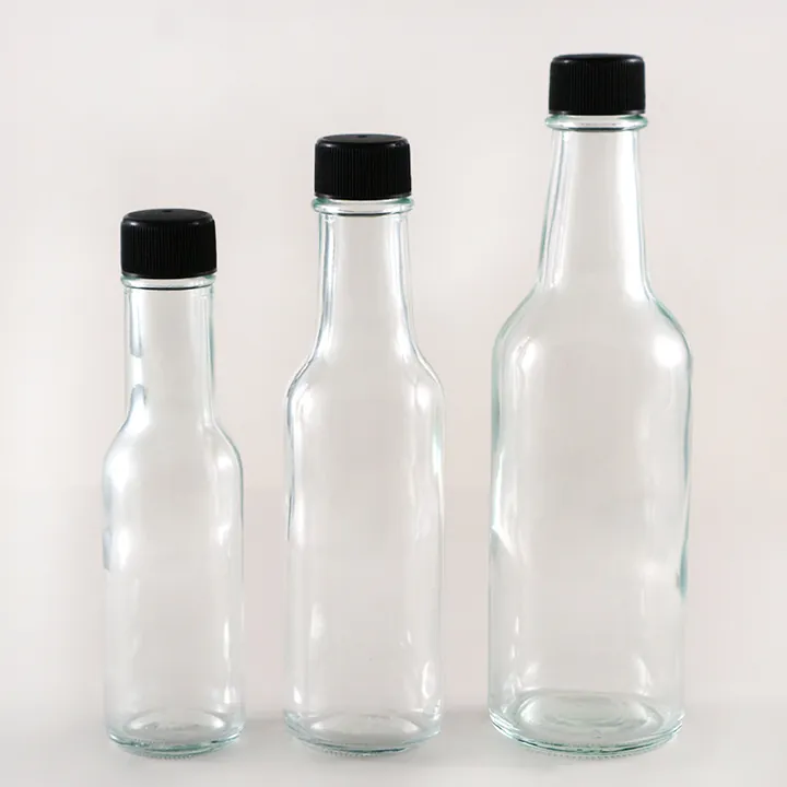 Three clear hot sauce bottles with black caps in different sizes
