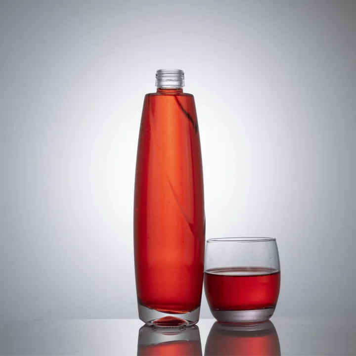 Schlanke Saftflasche aus klarem Glas mit rotem Getränk und Glasbecher